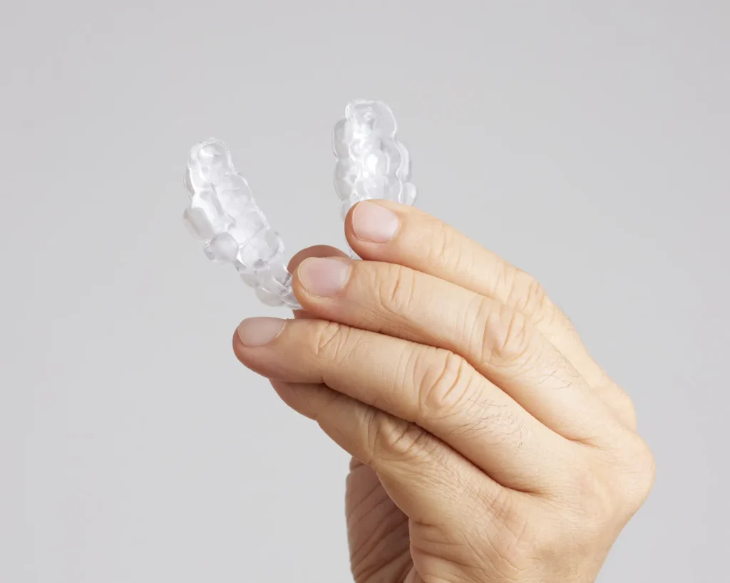 A hand holding two clear dental aligners—oral appliances often used for sleep apnea or snoring relief—against a plain light gray background.