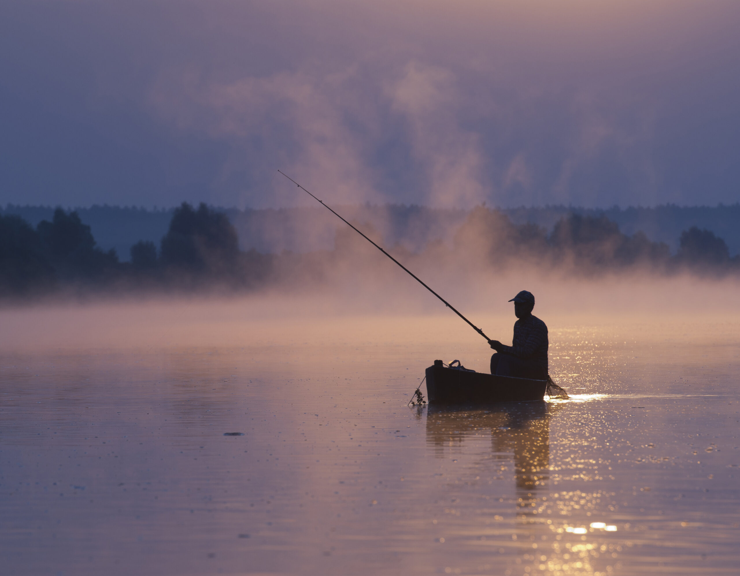 Une personne dans un petit bateau pêche sur un lac calme au lever du soleil, entouré de brume et de lumière douce - une scène paisible qui ressemble à un traitement contre l'insomnie, avec des arbres faiblement visibles à l'arrière-plan.