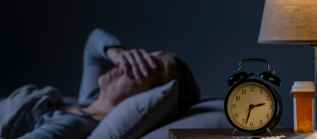 Person struggling to sleep at night with alarm clock and medication on bedside table