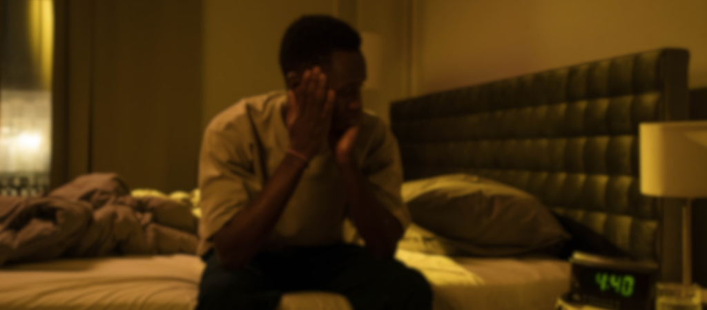 Person sitting awake in bed at night with a glowing alarm clock, illustrating insomnia symptoms.