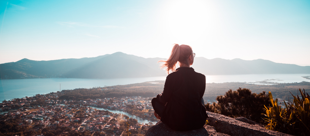 Person sitting on a hill overlooking a city and lake, representing reflection on ADHD, sleep difficulties, and mental well‑being.