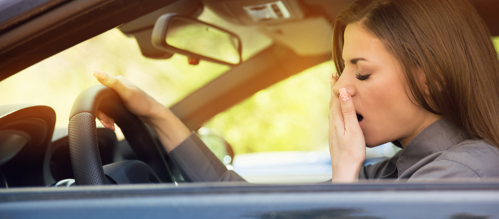 Person yawning while sitting in a car, illustrating daytime fatigue and low energy associated with sleep loss and weight challenges in women.