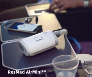 ResMed AirMini travel CPAP machine on an airplane tray table, illustrating lightweight CPAP use during air travel.